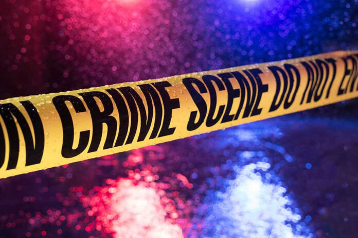 Yellow crime scene tape with police lights in background.