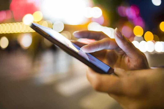 A persons hand using a smartphone in a city at night with blurred lights in the background