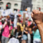Leftist Protestors Unveil NEW Anti-ICE Tactic Raised fist in front of a crowd.