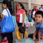 People waiting outside carrying bags, boys sitting and playing.