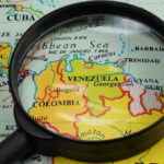 Delta Force DRAGS Dictator From Bedroom Magnifying glass focusing on Venezuela and Colombia on map.