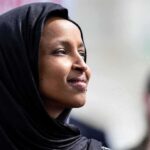 A woman wearing a black hijab looking thoughtfully during an outdoor event