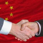Two hands shaking in front of the Chinese flag