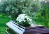 Coffin with white flowers outdoors in green surroundings.