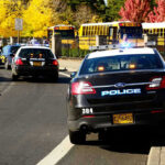 Trans Teacher LEAKS School Kill List Police cars and school buses on a road.