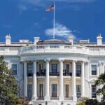 The White House with the American flag flying against a blue sky