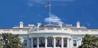The White House with the American flag flying against a blue sky