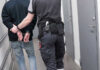 Highway Sting Nabs 249 Illegal Immigrants Officer escorting handcuffed person down hallway.