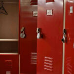 Teacher’s Pen Camera SHOCKER – Schools in Crisis Red lockers with padlocks, one open with hanger.