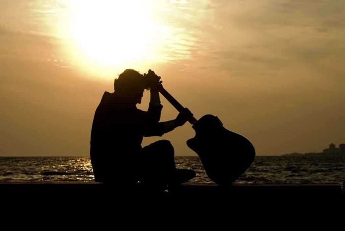 Silhouette of a guitarist sitting by the ocean during sunset