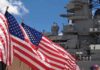 American flags in front of a naval ship under a blue sky