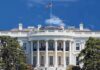 The White House with the American flag flying against a blue sky