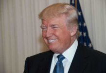 A smiling man in formal attire with an American flag in the background