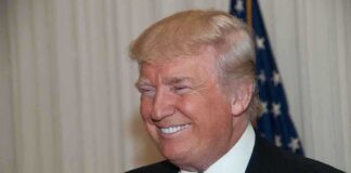 A smiling man in formal attire with an American flag in the background