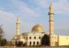Mosque with golden dome and two tall minarets under a partly cloudy sky