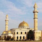 Mosque with golden dome and two tall minarets under a partly cloudy sky