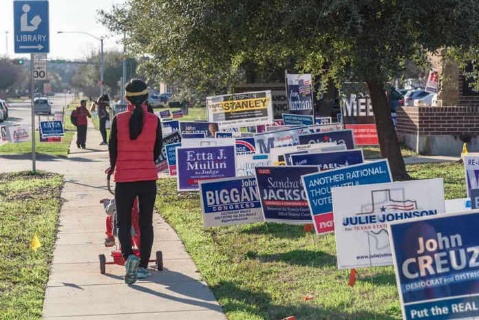Person walking with stroller past numerous election campaign signs.