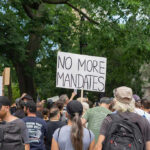 Crowd holds No More Mandates sign at protest.
