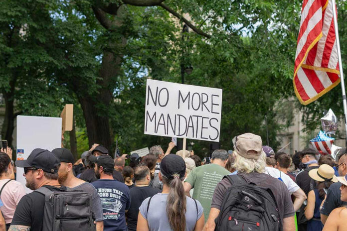 Crowd holds No More Mandates sign at protest.