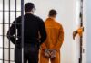 American Cop ARRESTED Over Russian Spy Allegations! Prisoner in orange jumpsuit handcuffed and escorted by officer
