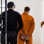 American Cop ARRESTED Over Russian Spy Allegations! Prisoner in orange jumpsuit handcuffed and escorted by officer