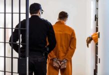 American Cop ARRESTED Over Russian Spy Allegations! Prisoner in orange jumpsuit handcuffed and escorted by officer