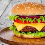 Burger Icon Closes Hundreds of Locations – Beef Crisis! Cheeseburger with lettuce, tomato, and onion on a wooden plate