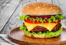 Burger Icon Closes Hundreds of Locations – Beef Crisis! Cheeseburger with lettuce, tomato, and onion on a wooden plate