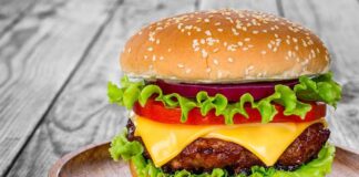 Cheeseburger with lettuce, tomato, and onion on a wooden plate