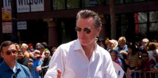 Gavin Newsom gives a thumbs-up at a parade; Teddy Williams stands nearby in a crowd