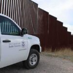 Border patrol SUV parked beside tall steel border fence