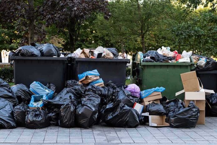 shutterstock_1509489287 Overflowing dumpsters with piles of trash bags and cardboard