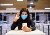 Woman in face mask video calling on smartphone in a cafeteria