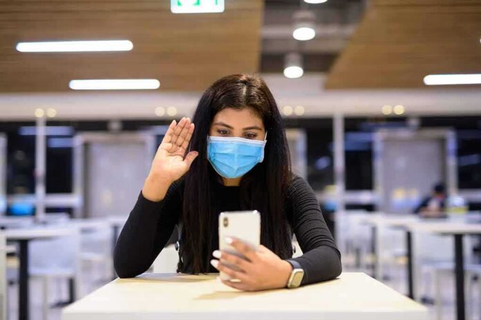 shutterstock_1734271934 Woman in face mask video calling on smartphone in a cafeteria