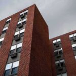 Brick apartment buildings with window air conditioners under cloudy sky
