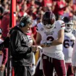 Mississippi State football coach and quarterback review play card on sideline