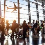 Passengers queue inside an airport terminal at sunset