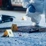 Forensic investigator examines a crime scene with evidence markers and a handgun