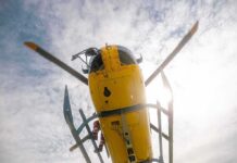Yellow helicopter seen from below with spinning rotor against a bright sky