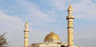 Mosque with golden dome and two tall minarets under a partly cloudy sky