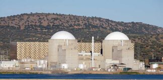 Nuclear power plant with domed structures beside a water body and mountains in the background