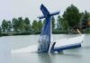 A submerged airplane partially in a lake with trees in the background
