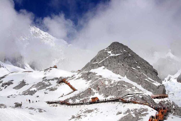 Snow-covered mountain with hiking trails and tourists under a cloudy sky