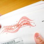 A hand holding an envelope labeled Official Election Mail