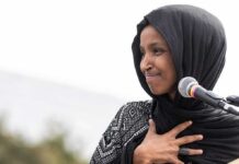 Lefty’s Throw a Massive Hissy Fit After Omar’s Home Gets Raided Ilhan Omar speaking at a microphone with hand on chest