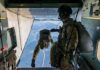 Paratroopers jump from a military aircraft over coastline