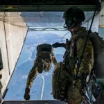 Paratroopers jump from a military aircraft over coastline
