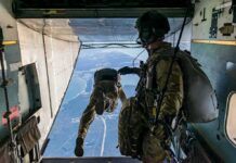 Paratroopers jump from a military aircraft over coastline