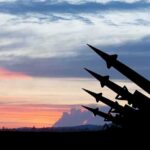 Silhouetted missiles on launchers against a colorful sunset sky