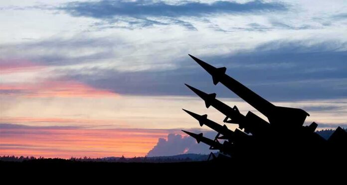 shutterstock_2265396937 Silhouetted missiles on launchers against a colorful sunset sky